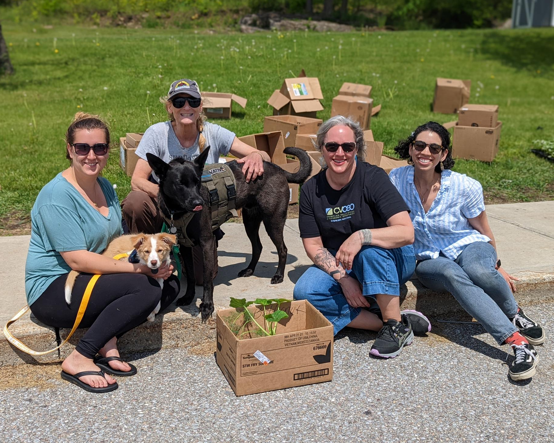 Staff and volunteers sit together at 2022 Garden Day holding free seedlings and their dogs.