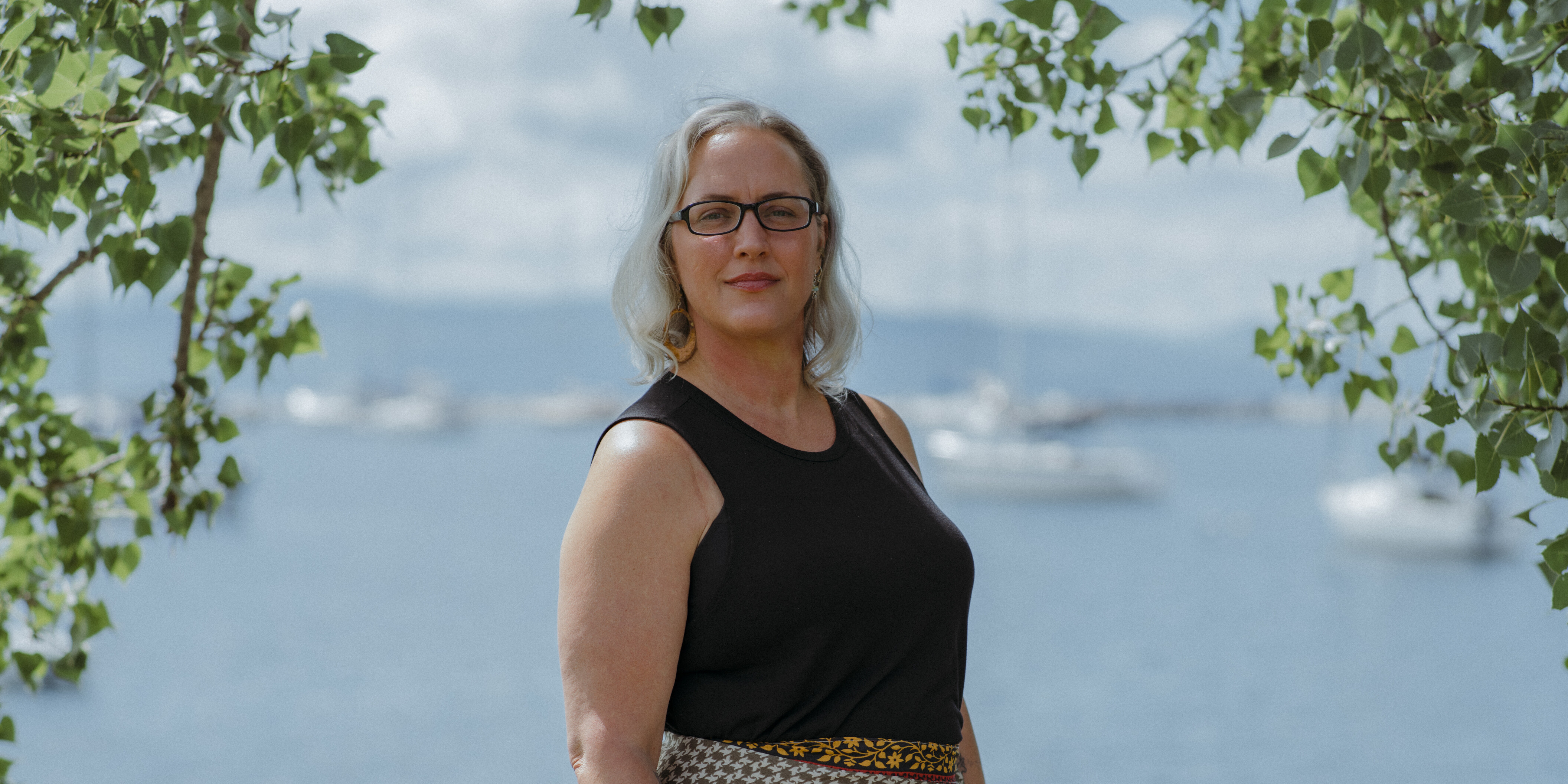 Toni portrait, black shirt and glasses, faded background of Lake Champlain.